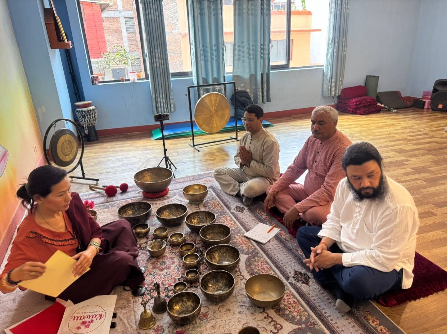 A group class in progress — students sitting in meditation around a full set of singing bowls and two gongs